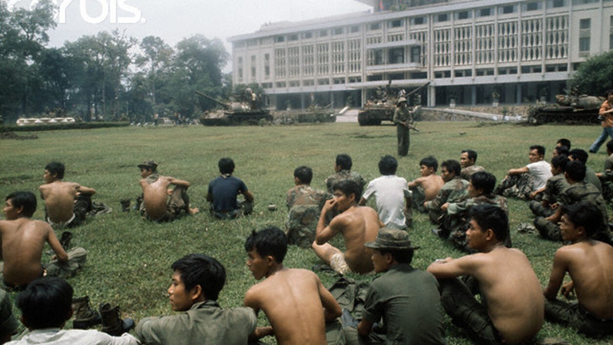 Captured South Vietnamese soldiers sit on a broad lawn after North Vietnamese troops seize the presidential palace in Saigon